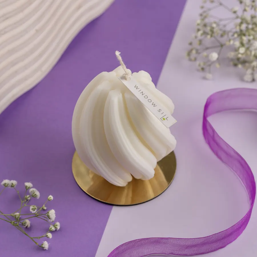 White Twirl Candle by Windowsill on a gold stand, with purple ribbon and baby’s breath, showcasing aesthetic decor.