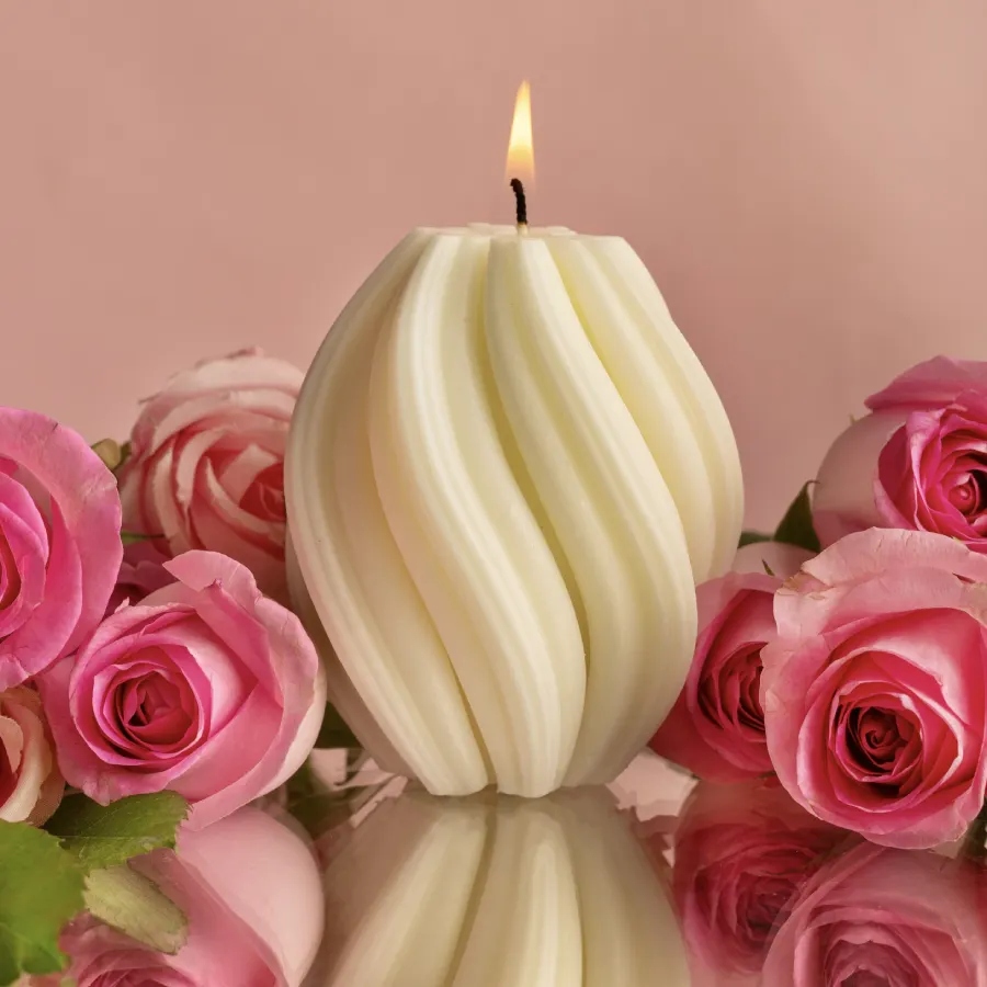 Lit white Twirl Candle by Windowsill, surrounded by pink roses on a reflective surface, showcasing elegant decor.